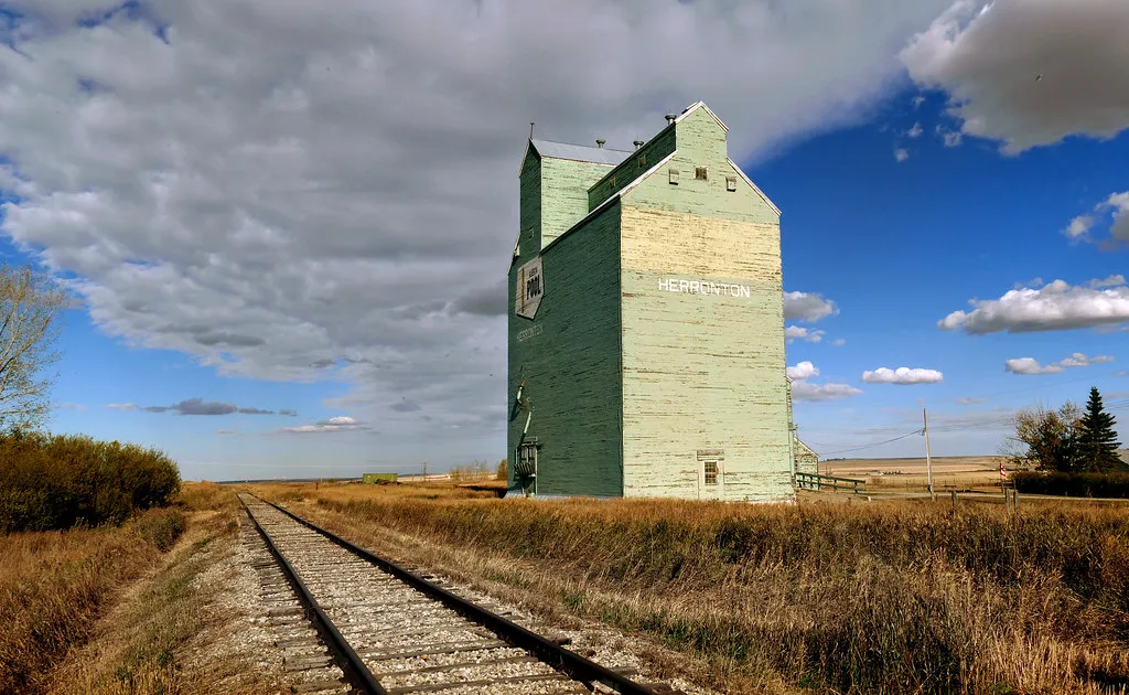 A wooden grain elevator beside a railway line on open, flat farmland